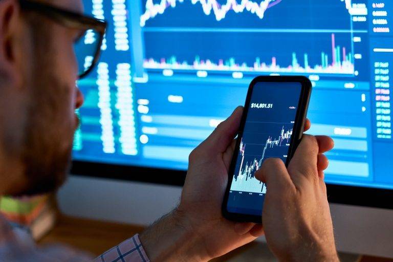 Trader using mobile phone app analytics for stock trading graph data analysis.